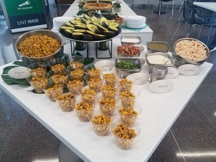 An elote and avocado bar with small cups and toppings laid out