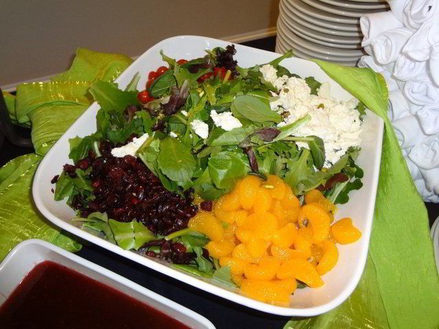 A large tray of mixed green salad with fruit and cheese
