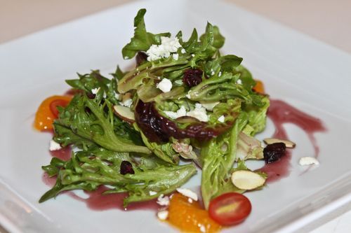 A mixed green salad with feta, almonds and tomatoes on a white plate