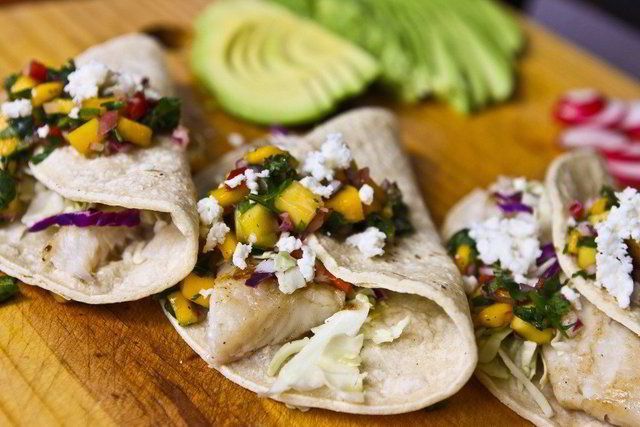 Fish tacos topped with mango salsa on a wooden board