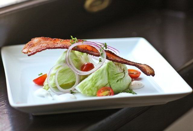 A wedge salad with bacon, tomato and red onion on a square plate